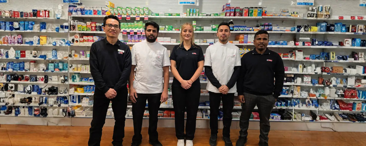 Five people standing in a pharmacy with shelves stocked with products in the background