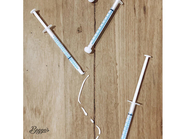 Four syringes containing Bagga's Eyeliner Numbing Gel arranged on a wooden surface, with a small amount of gel dispensed in the center, showcasing expert medication support.